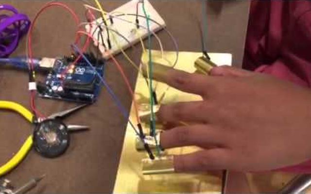 Video still: a hand wearing brass finger contacts wired to an Arduino