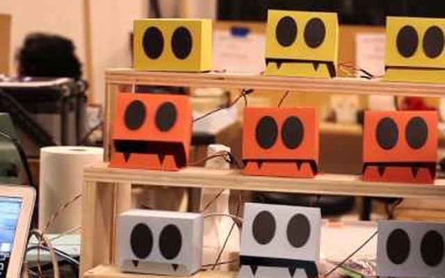Video still: shelves of small colored boxes with cartoon eyes