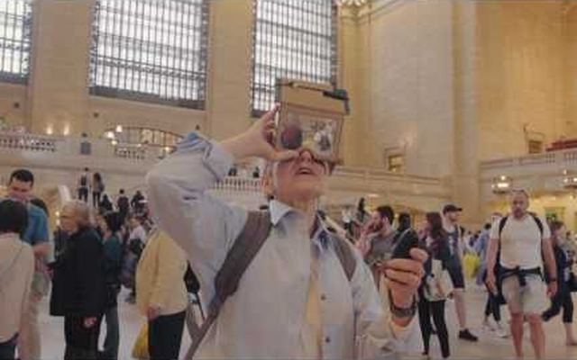 Video still: a person in Grand Central Terminal wearing a cardboard HoloKit headset