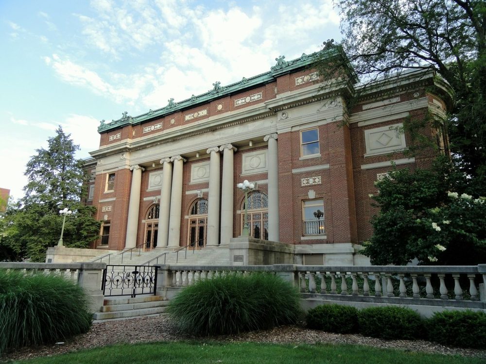 Photograph of Foellinger Auditorium: a red brick building with a wide low dome, a green copper cornice, limestone trim and four tall Ionic columns behind a stone balustrade.